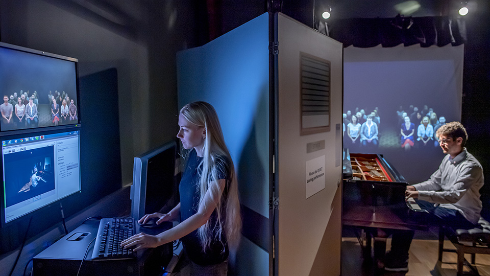 A student performing on a pianist in front of a visual simulator, with a women managing the simulator on screens.